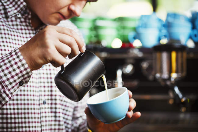 Mann gießt heiße Milch in eine Tasse Kaffee — Stockfoto