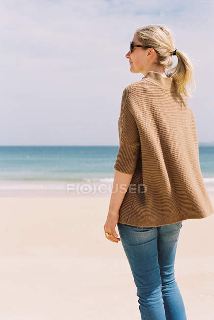 Femme dans une veste brune debout sur la plage — Photo de stock