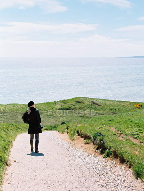 Mujer de pie en un camino de acantilado mirando hacia fuera - foto de stock