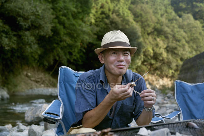 Uomo mangiare un pesce alla griglia al picnic — Foto stock