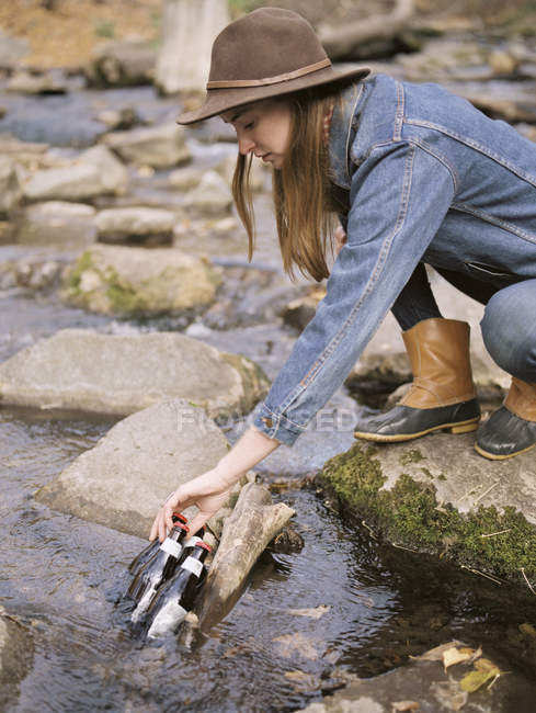 Mujer poniendo botellas de bebida en un río . - foto de stock