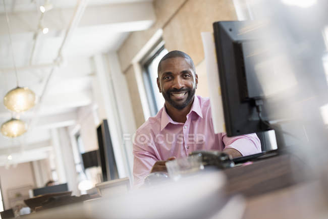 Uomo seduto a una scrivania da un monitor del computer . — Foto stock