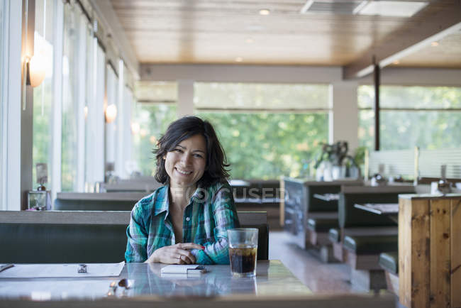 Frau im karierten Hemd sitzt an einem Tisch — Stockfoto