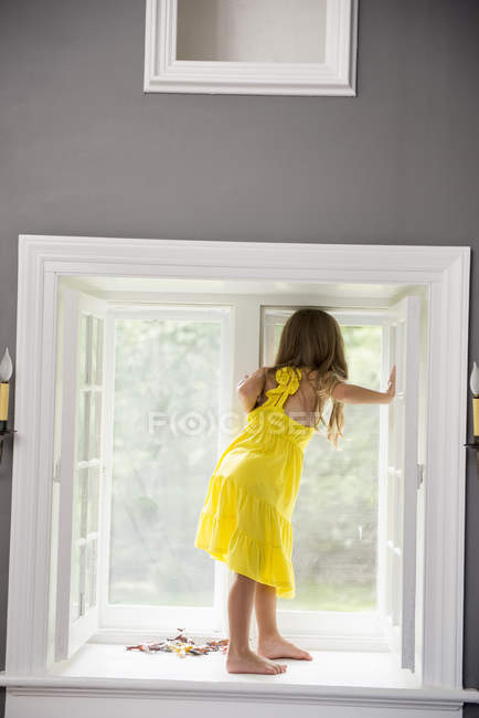 Menina sentada por uma janela jogando . — Fotografia de Stock