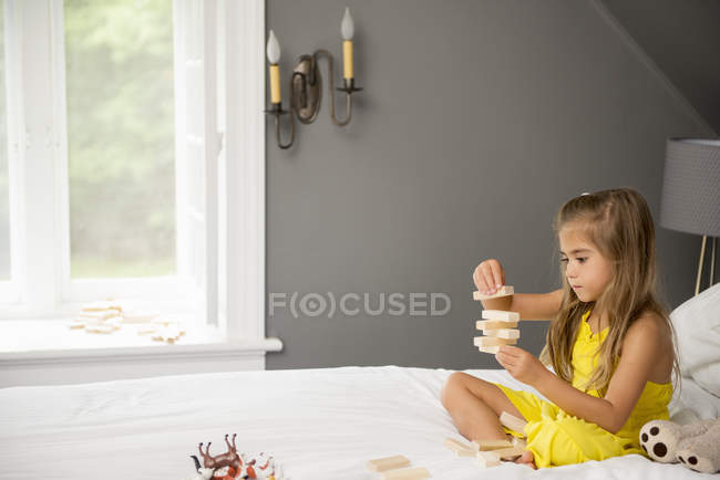 Chica sentada en una cama, jugando - foto de stock