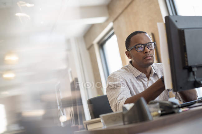 Homem sentado em uma mesa usando um computador . — Fotografia de Stock