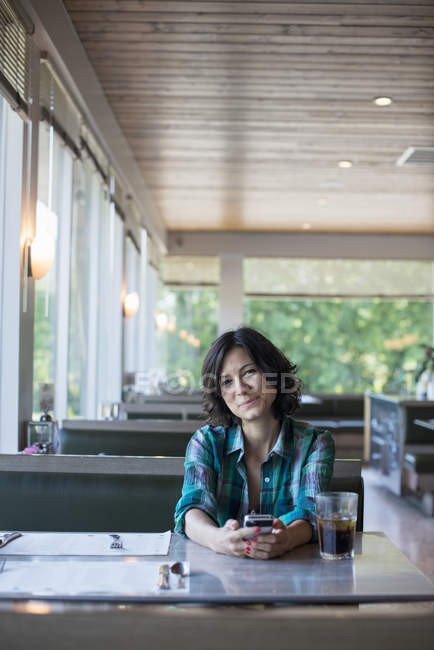 Жінка дивиться на свій смартфон за столом — стокове фото