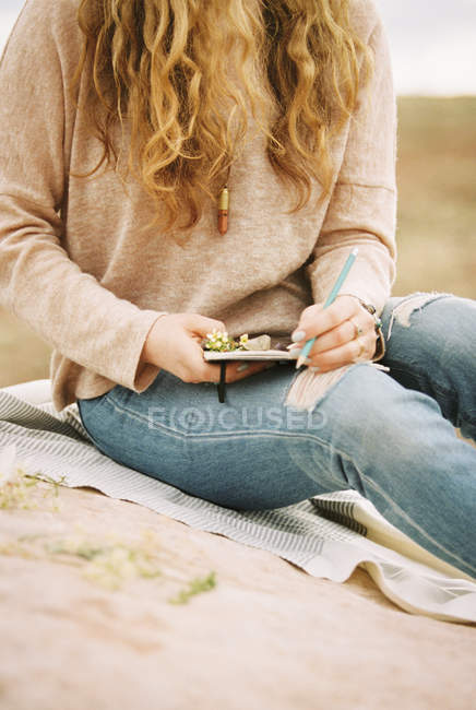 Mujer sentada en una roca, sosteniendo un cuaderno - foto de stock