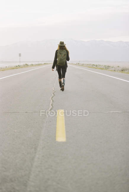 Mulher com mochila caminhando estrada país — Fotografia de Stock