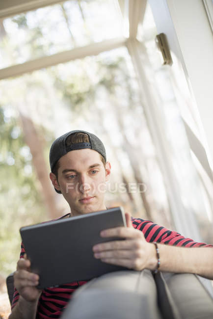Чоловік сидить на дивані, з цифровим планшетом — стокове фото