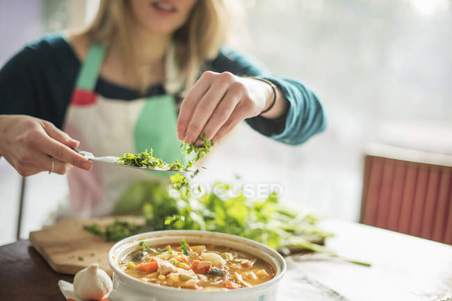 Woman sprinkling herbs into vegetable stew — Stock Photo