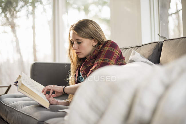 Young woman reading book on sofa — Stock Photo