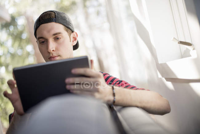 Человек сидит на диване, с цифровым планшетом — стоковое фото