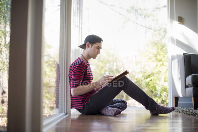 Человек, сидящий на полу, с цифровым планшетом — стоковое фото