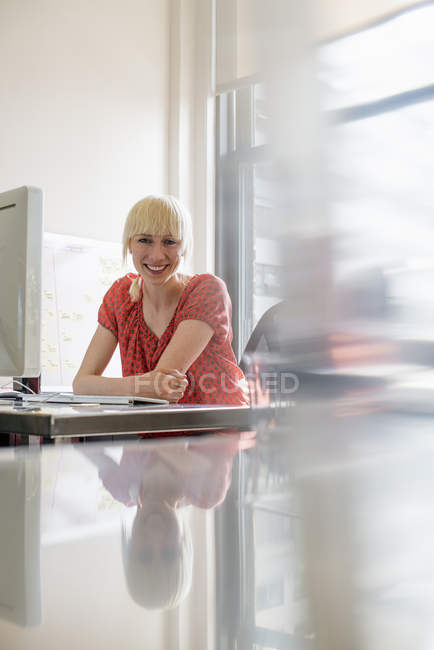 Frau sitzt lächelnd am Schreibtisch. — Stockfoto