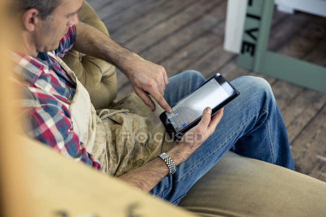 Möbelrestaurator sitzt und blickt auf ein digitales Tablet — Stockfoto