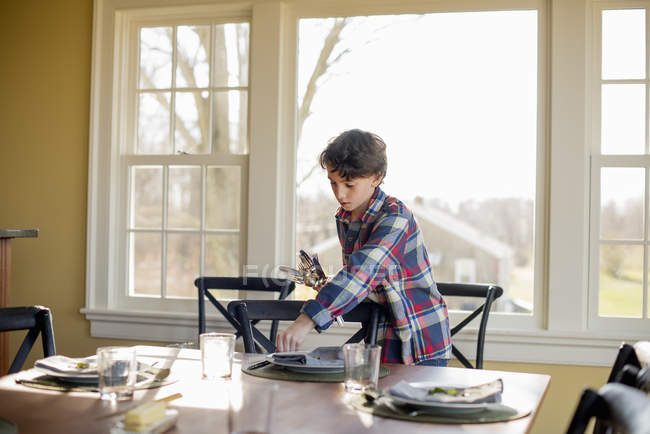 Boy setting the table with cutlery and glasses — Stock Photo