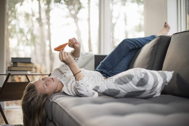 Girl on sofa, holding paper bird. — Stock Photo