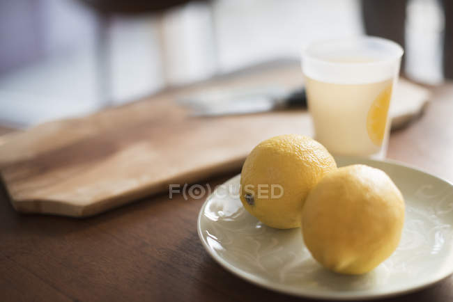 Planche à découper avec couteau, assiette avec citrons — Photo de stock