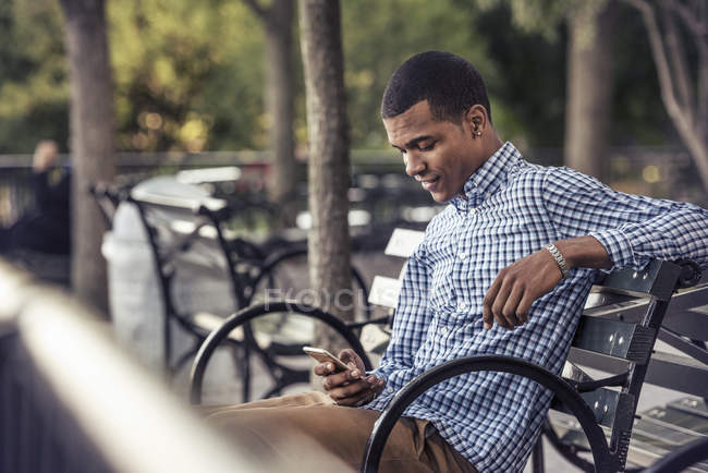 Homem em um parque olhando para um telefone inteligente — Fotografia de Stock