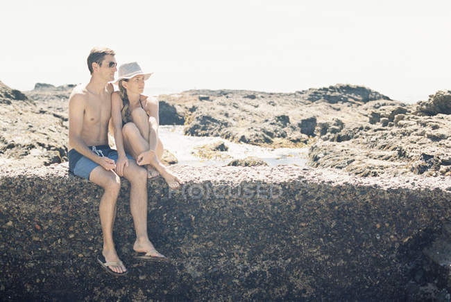 Casal na praia sentado em uma parede — Fotografia de Stock