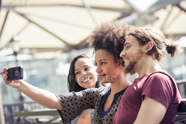 Homem e duas mulheres tomando selfies em um parque da cidade — Fotografia de Stock