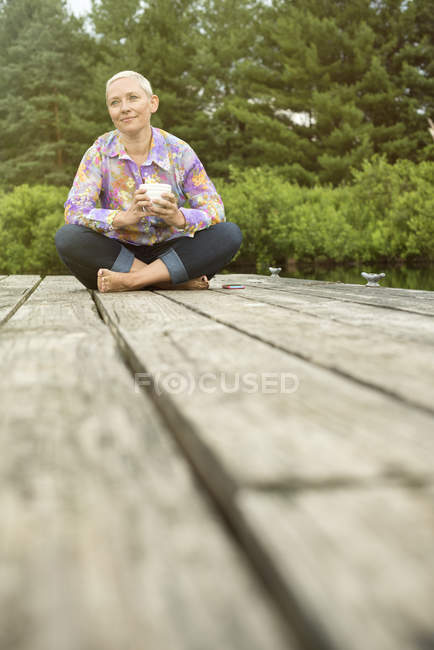 Жінка сидить на причалі з чашкою кави — стокове фото