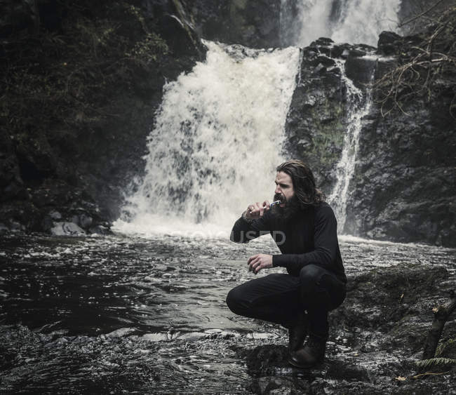 Man cleaning teeth by a flowin stream. — Stock Photo