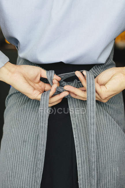 Garçonete jovem amarrando seu avental — Fotografia de Stock