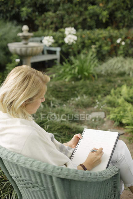 Mulher sentada em um jardim, escrevendo . — Fotografia de Stock