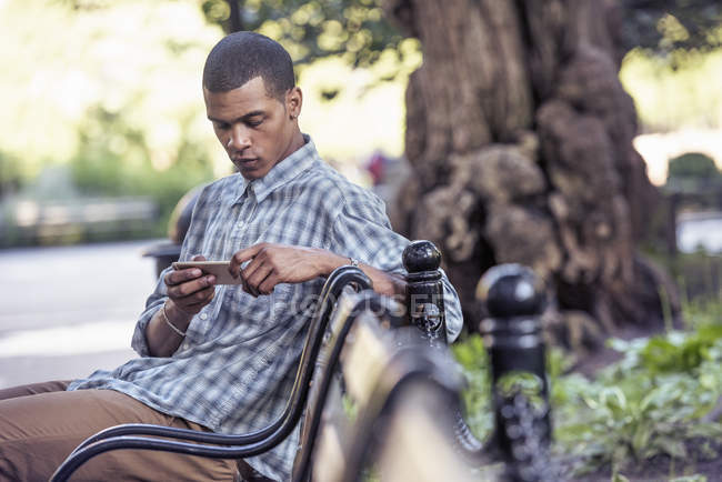 Uomo che utilizza il suo smartphone su panchina — Foto stock