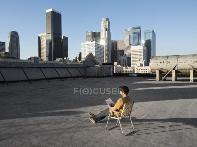 Man on a city rooftop reading. — Stock Photo