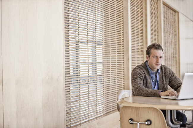 Hombre sentado en la oficina, mirando el ordenador portátil - foto de stock
