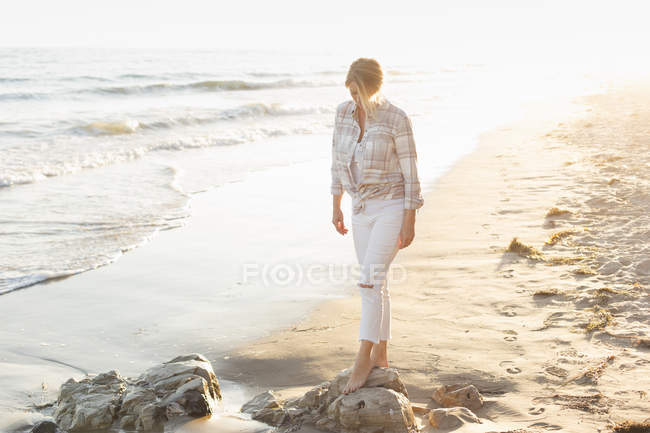 Mulher andando ao longo de uma praia arenosa — Fotografia de Stock