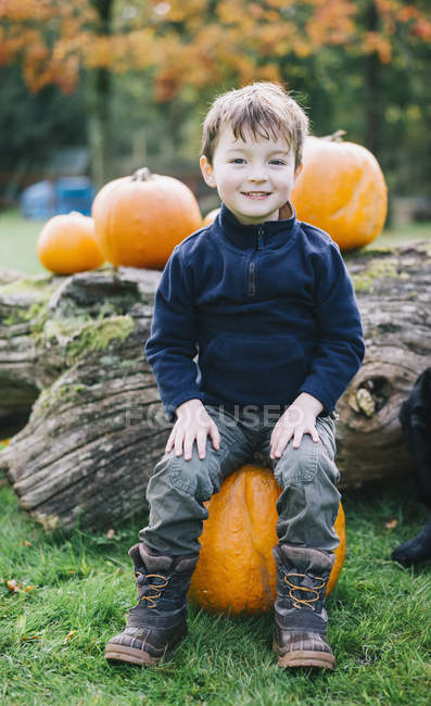 Menino sentado em uma grande abóbora laranja — Fotografia de Stock