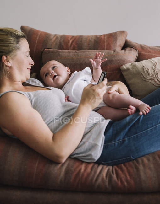 Woman lying on a sofa with baby girl. — Stock Photo