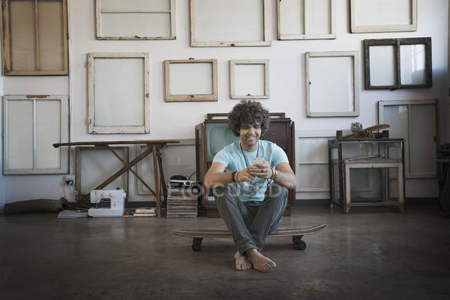 Mann sitzt auf Skateboard und checkt Handy — Stockfoto
