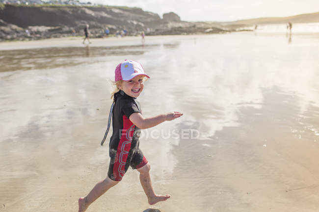 Criança em um terno de mergulho que corre na areia — Fotografia de Stock