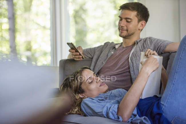 Hombre revisando su teléfono y mujer leyendo un libro - foto de stock