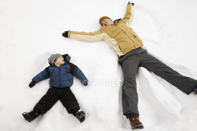 Uomo e bambino fare neve angelo forme . — Foto stock
