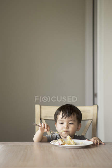 Jeune garçon assis sur une chaise à une table — Photo de stock