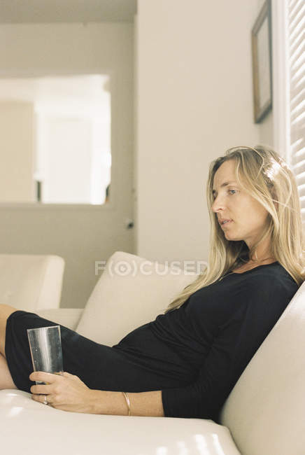 Woman sitting on a sofa, holding a glass. — Stock Photo