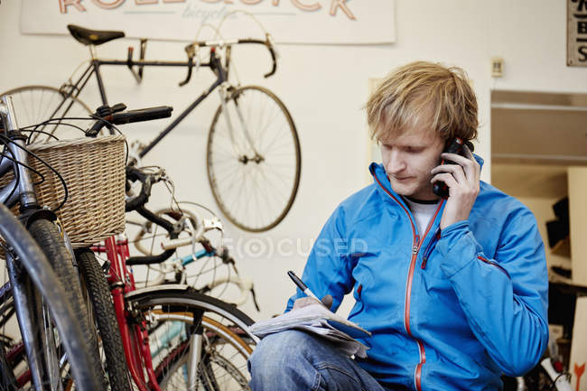 Hombre haciendo una llamada en una tienda de bicicletas - foto de stock