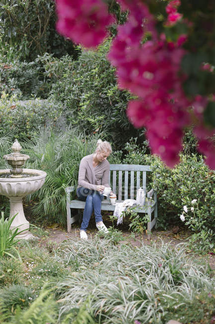 Femme assise sur un banc en bois dans un jardin — Photo de stock