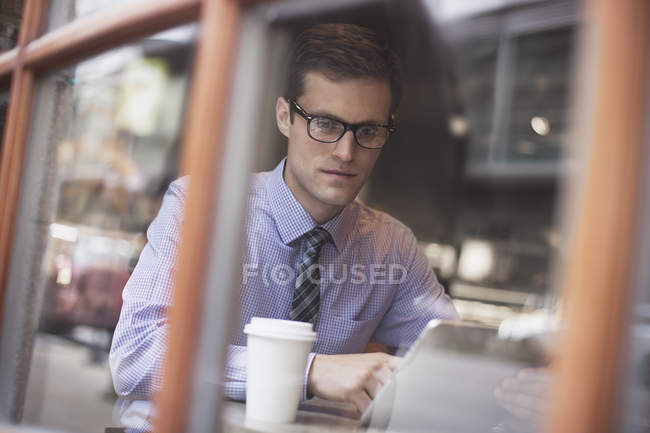 Empresario sentado en una cafetería, usando laptop - foto de stock