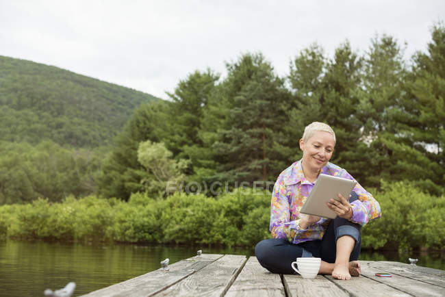 Frau sitzt mit Tablet auf Steg — Stockfoto