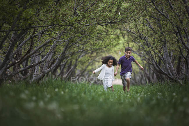 Children running along tree branch tunnel — Stock Photo