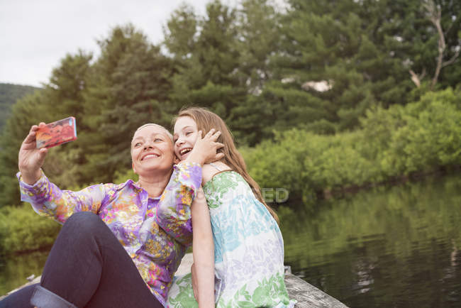 Mulher e uma criança na doca do lago tomando uma selfie — Fotografia de Stock