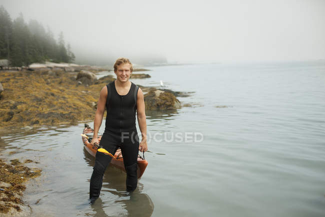 Man in a wetsuit drawing his kayak — Stock Photo
