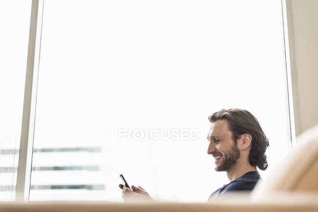 Homem sentado verificando seu telefone inteligente — Fotografia de Stock